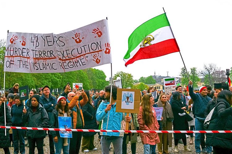 Demonstranten und Demonstrantinnen halten eine iranische Flagge in die Höhe.