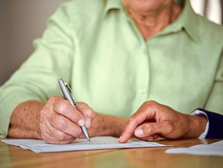Ältere Frau unterschreibt Dokument.