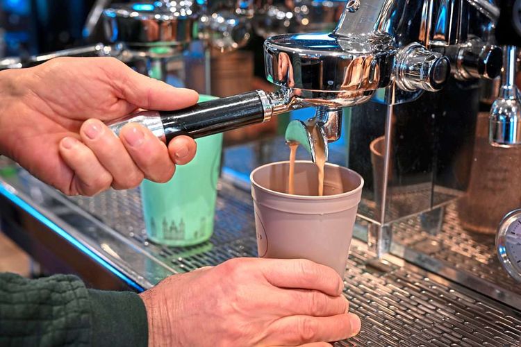 Ein Mitarbeiter eines Bio-Ladens bereitet einen Kaffee zu, der in einen Mehrwegbecher fließt.