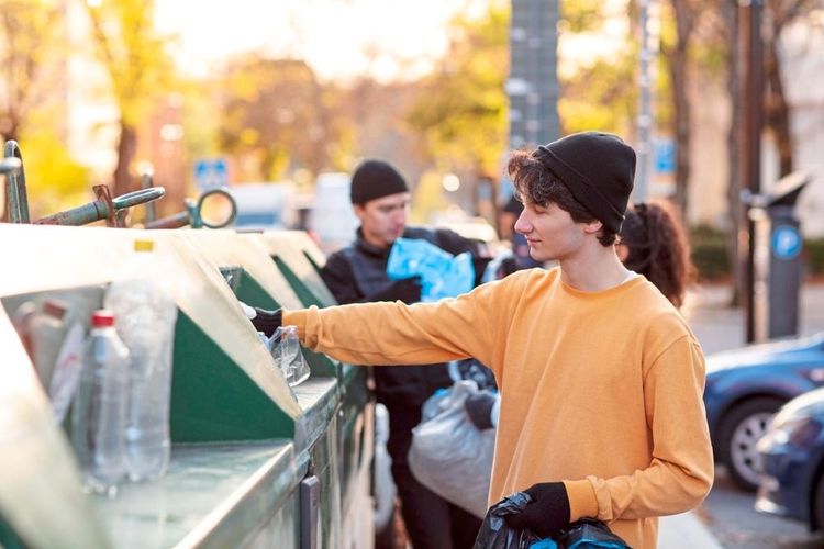 Ein junger Mann wirft eine Plastikflasche in einen Recyclingcontainer.