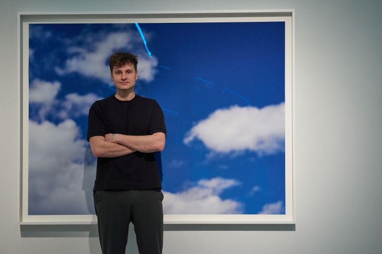 Der Künstler vor einem Wolkenfoto.