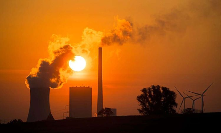 Ein Kohlekraftwerk in Deutschland im Sonnenuntergang, rechts davon stehen eine Windräder.