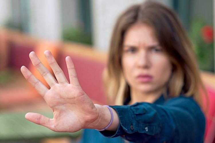 Eine Frau hält mit kritischem Blick eine Hand in einer stoppenden Geste hoch