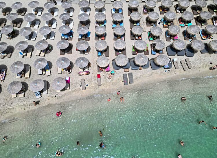 Ein griechischer Strand mit Reihen an Sonnenschirmen.