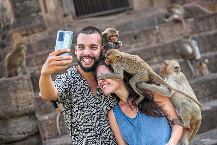 Ein Mann macht ein Selfie, während Affen über ihn und eine an ihn geschmiegte Frau klettern.