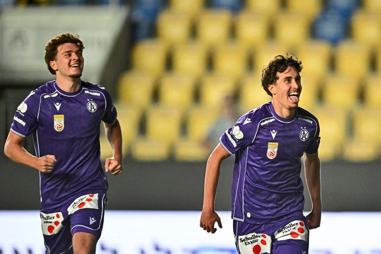 Zwei Fußballspieler des Teams Austria Wien in violetten Trikots feiern auf dem Spielfeld. Im Hintergrund sind leere gelbe und blaue Tribünenplätze sichtbar.