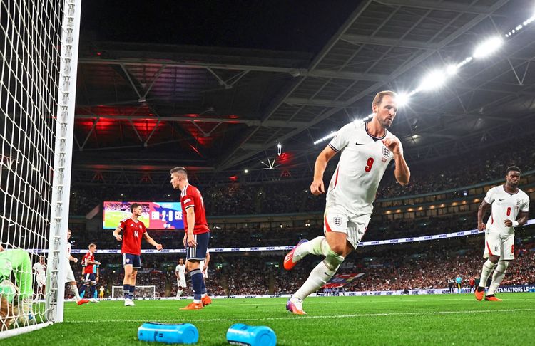 Ein Fußballspieler im weißen Trikot der englischen Nationalmannschaft feiert ein Tor während eines Spiels im Wembley-Stadion. Im Hintergrund stehen Spieler der gegnerischen Mannschaft, einige schauen enttäuscht. Der Spielstand zeigt 3:1. Zuschauer füllen das Stadion bei Nachtbeleuchtung.