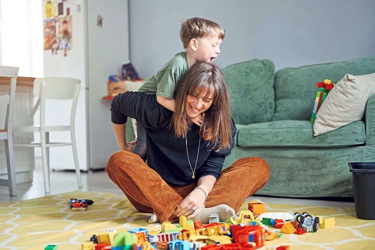 Eine Mutter spielt mit ihrem kleinen Sohn im Wohnzimmer am Boden Duplo Lego
