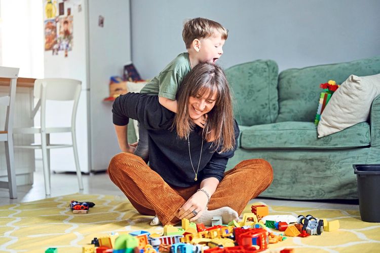 Eine Mutter spielt mit ihrem kleinen Sohn im Wohnzimmer am Boden Duplo Lego