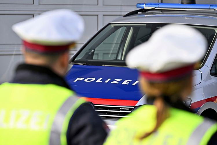 Ein Polizist und eine Polizistin in gelben Warnwesten stehen vor einem Polizeifahrzeug mit der Aufschrift 