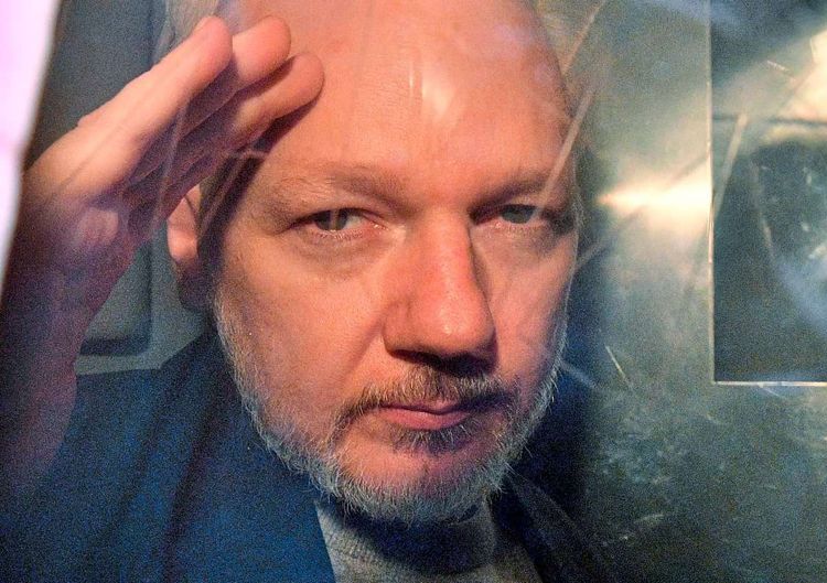 Julian Assange schaut durch ein Fenster.