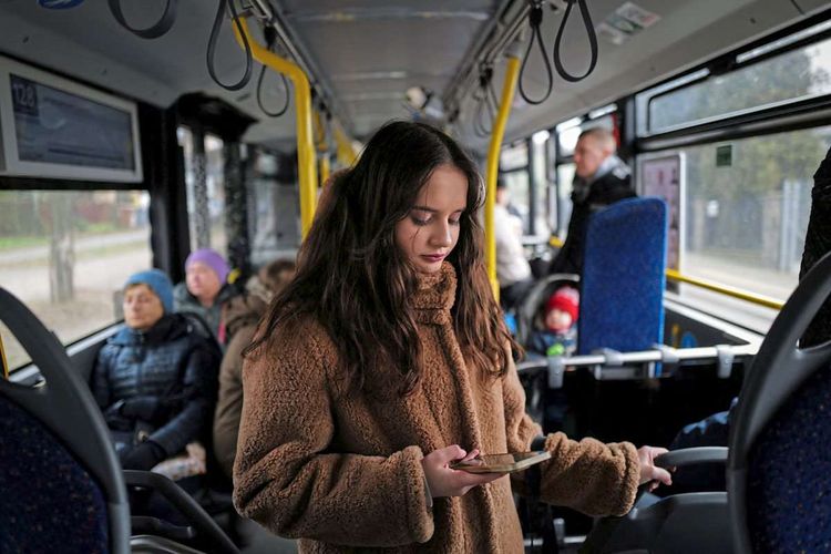 Jugendliche steht in einem Bus und schaut auf ihr Smartphone