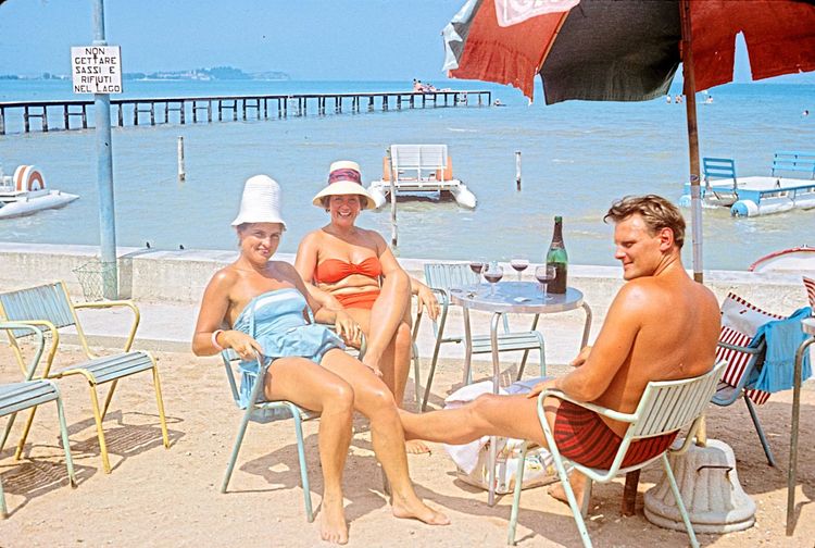 Eine Retro-Aufnahme von Touristen in Strandbekleidung an einem Tischchen mit Weingläsern.