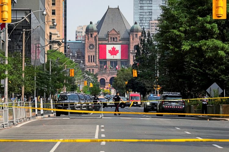 Absperrband sperrt die Straße vor dem Parlamentsgebäude in Toronto, Kanada, ab, während Polizeiautos und Einsatzkräfte am Tatort eines Vorfalls präsent sind. Im Hintergrund ist eine große kanadische Flagge am Gebäude sichtbar.