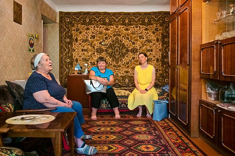 Sozialarbeiterin Valentina Bobrenko (Mitte) und ihre Klientin Valentina Gritsai (links) sitzen mit einer dritten Person im Wohnzimmer.