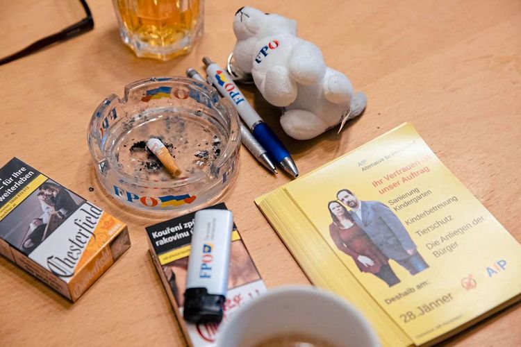 Auf einem Tisch liegen Zigarettenpackungen, ein FPÖ-Aschenbecher, ein FPÖ-Feuerzeug, FPÖ-Kugelschreiber, ein FPÖ-Schlüsselanhänger aus Plüsch und Flyer der 