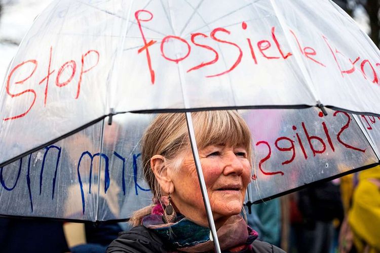Eine Frau steht mit einem Regenschirm, auf dem Slogans geschrieben stehen, auf einer Klimademonstration.